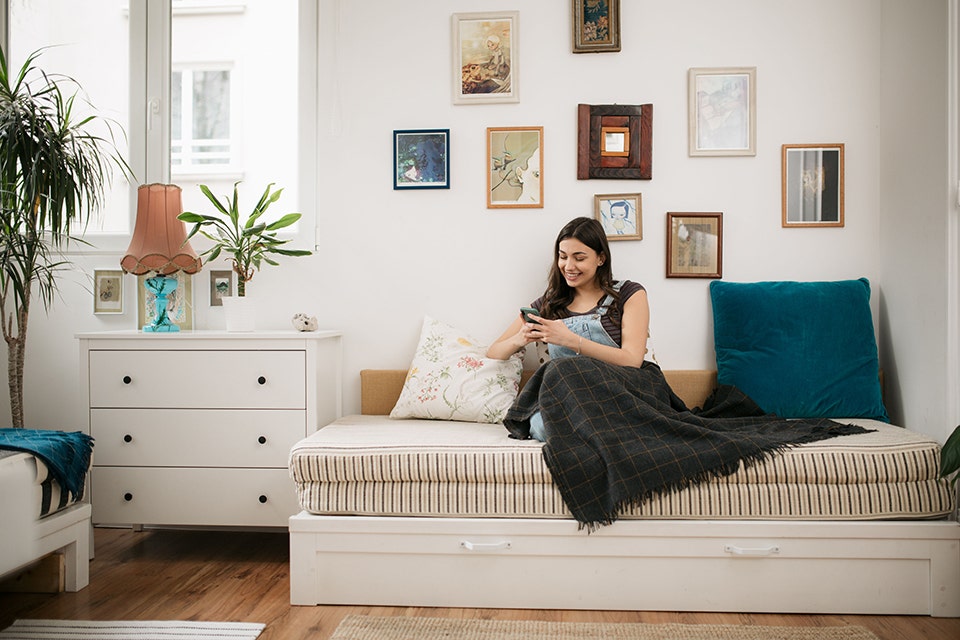 A woman reclining comfortably on a diwan, scrolling her phone.