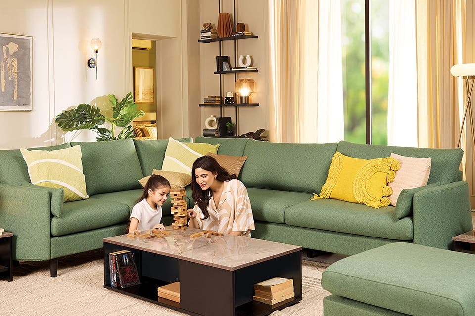 A mother and her child sitting beside a rectangular coffee table in front of a sectional sofa in a contemporary living room.