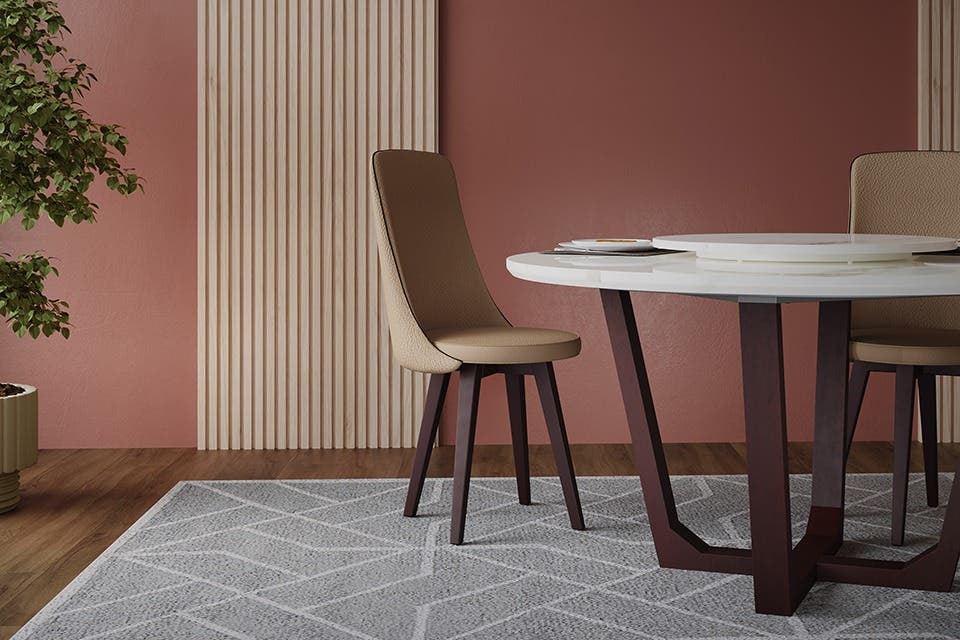The edge of a sleek round dining table with a chair, along with a houseplant and a rug.
