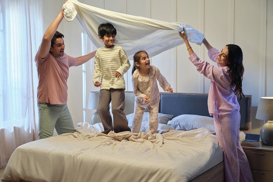  Two kids playing on a bed while their parents join in from either side. 