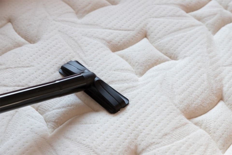 A handheld vacuum attachment to remove dust and allergens on a quilted mattress. 