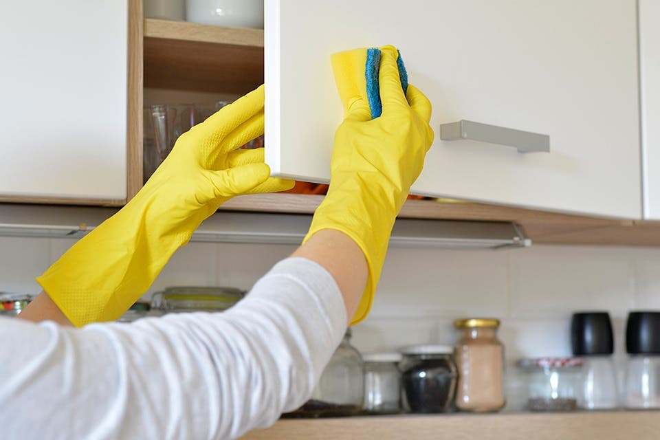 Close-up of a person wiping down a modular kitchen cabinet.
