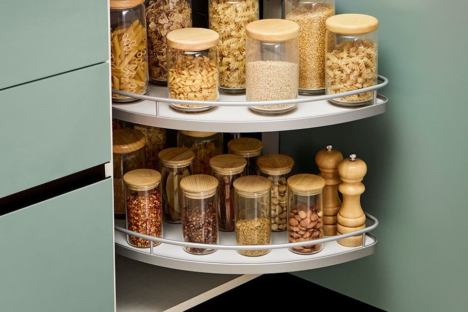Modular kitchen corner cabinet with rotating Lazy Susan shelves holding stainless steel cookware for easy access.