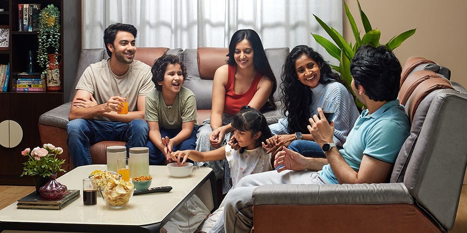 Person comfortably seated in a recliner sofa watching television with family.