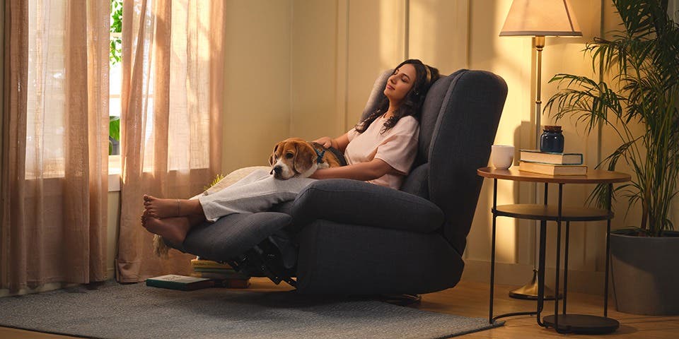 Person relaxing with a dog on a contemporary recliner with a side table and floor lamp in a cosy living room.
