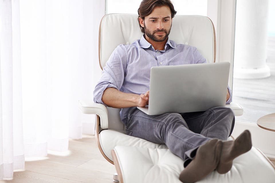 A person working on a laptop while seated in a recliner.