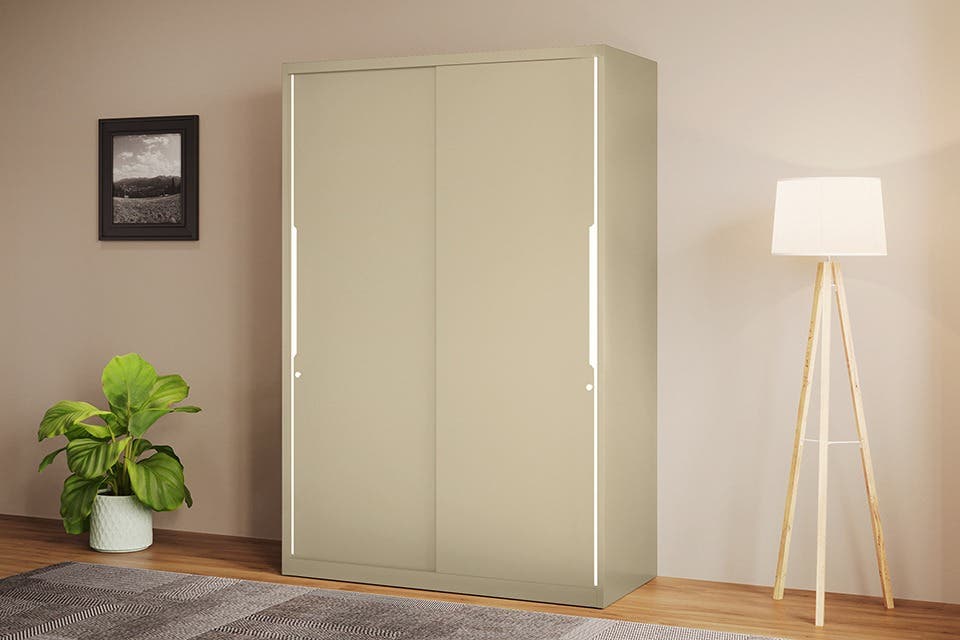 A sliding wardrobe placed alongside an indoor plant, rug and lamp in a bright bedroom.