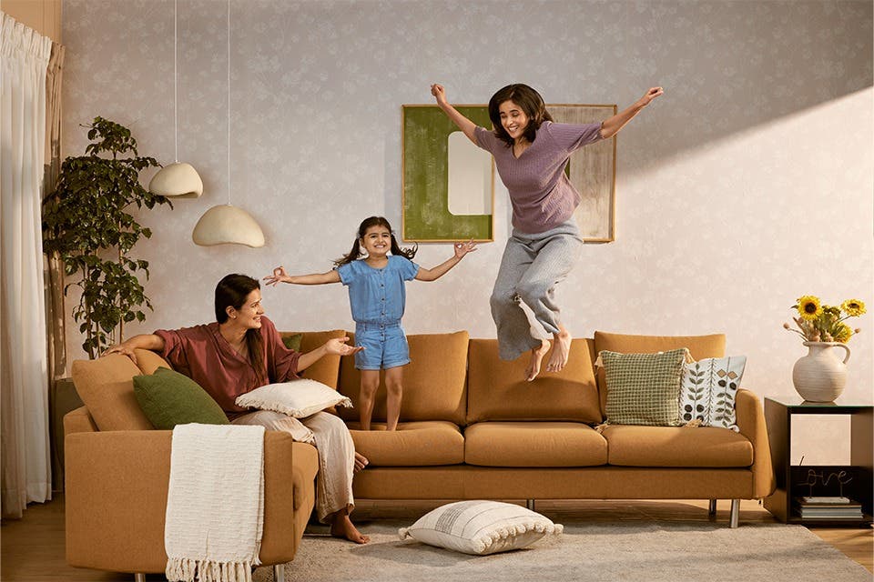 People and a child jumping around on a fabric sofa covered with performance fabric in a kid-friendly home.