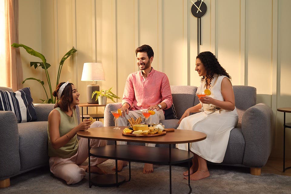 People laughing in a contemporary living room with a sofa set, coffee table and house plants.